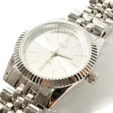 Reloj de pulsera plateado con caja redonda, dial plateado con agujas e indicadores horarios en plateado y pulsera de eslabones metálicos.