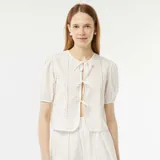 Blusa blanca con mangas cortas abullonadas y detalle de calado. Tiene escote redondo y cierre frontal con cintas.