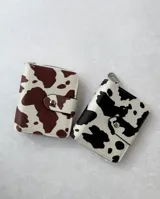 Billetera pequeña con estampado de vaca en blanco y negro o blanco y marrón, con cierre de broche y compartimentos para tarjetas, billetes y monedas.