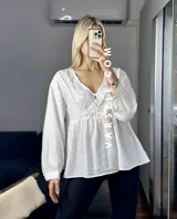 Blusa color crema con escote en V, mangas largas abullonadas con puños elásticos y detalles de encaje y bordado en el frente.