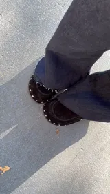 Zuecos de gamuza color marrón chocolate, con base de goma negra, tachas plateadas alrededor de la base y plantilla acolchada.