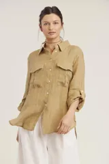 Camisa de lino color beige con cuello clásico, cierre frontal con botones, mangas largas con trabillas para enrollar y dos bolsillos con solapa en el pecho.
