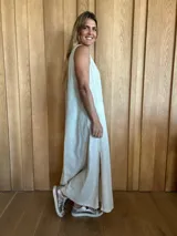 Vestido largo color crudo, sin mangas y con escote en V. Presenta aberturas laterales en el ruedo y bolsillos laterales a la altura de la cadera.