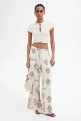 Pantalón de corte holgado en tejido liviano de mezcla de lino y viscosa, color crudo con estampado paisley en marrón. Modelo con cintura elástica fruncida y cordón para ajustar, bolsillos laterales discretos y piernas rectas con bajo deshilachado.