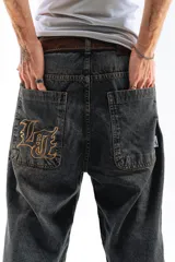 Pantalón de jean azul desgastado, corte mega baggy, con bordado dorado en el bolsillo trasero y botones personalizados.