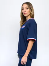 Remera blanca de corte clásico con cuello redondo y mangas cortas con puños tricolor (azul, blanco y rojo). Presenta el logo de Umbro bordado en el pecho izquierdo y el escudo del Club Nacional de Football bordado en el pecho derecho.