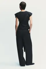Pantalón negro con finas rayas verticales blancas, de tiro alto y corte ancho. Incluye cinturón de lazo en el mismo tejido, bolsillos laterales y pinzas.