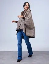 Ruana de tejido suave, color beige y marrón con estampado geométrico repetitivo. Posee cuello con aplique de piel sintética marrón y ribetes negros. Se combina con un suéter marrón de manga larga con botones en el puño.