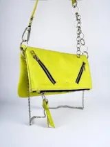 Cartera bandolera color amarillo flúor de cuero, con cierre superior y dos cierres diagonales decorativos en el frente. Tiene una correa de cuero regulable y una cadena metálica con aros.