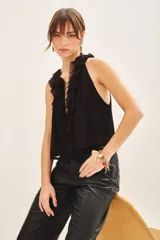 Blusa negra sin mangas, con escote en V profundo y volados en el frente. Tiene lazos en el cuello y gancho invisible para regular el escote.