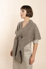 Chal asimétrico de lana color gris claro, con cortes en los hombros y doble ojal de fieltro para mantener el cruce. Terminación pespunteada y al corte.