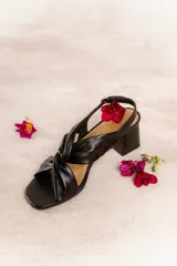 Sandalia de cuero color beige, con tiras anchas cruzadas y detalle de nudo central. Tiene pulsera regulable en el talón y taco ancho de 5,5 cm.