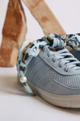 Zapatillas bajas de gamuza celeste con cordones y pañuelos estampados atados a los cordones.