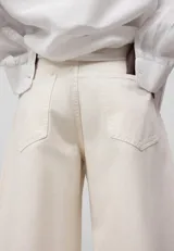 Pantalón cropped de denim de algodón color crudo, con trabillas, cierre con botón metálico, bolsillos delanteros y traseros, y pierna ancha acampanada en el bajo.
