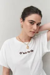 Remera blanca de manga corta con bordado frontal "C’est la vie", calce relajado y frunces laterales.