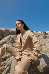 Blazer color beige confeccionado en lino, con solapas de muesca, cierre frontal con un botón y mangas largas con volantes en capas.