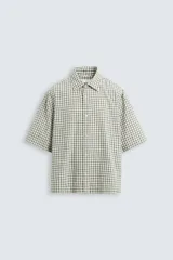 Camisa de hombre de corte boxy fit, confeccionada en tejido de algodón a cuadros en tonos beige, verde y azul. Tiene cuello solapa, manga corta y cierre frontal con botones.