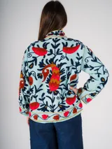 Chaqueta corta de color celeste con bordados florales en tonos rojos, naranjas, azules y negros.