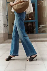 Jeans de tiro alto en denim de algodón rígido, color azul medio con efecto degradado (ombré) que se oscurece hacia el bajo. Corte acampanado (flare) y bajo deshilachado. Presenta bolsillos parche con botón en la parte delantera y trabillas ajustables con botón a los lados de la cintura.