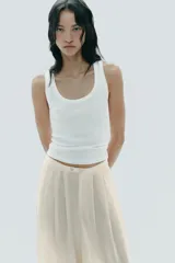 Pantalón palazzo color crudo, de tiro alto, confeccionado en lyocell. Presenta bolsillos laterales ocultos, detalle de pliegues en el delantero y cierre frontal con cremallera y botones.