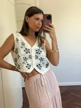 Chaleco tejido color crema con bordados florales en negro, escote en V y cierre frontal con botones.