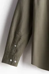 Camisa de algodón Oxford color verde oliva, de corte estándar, con cuello abotonado, tapeta clásica, bolsillo superior abierto, manga larga con puños abotonados y bajo levemente redondeado.