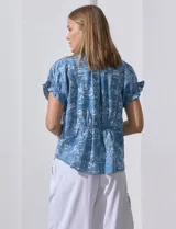 Blusa celeste estampada con motivos de playa, con cuello a la base y escote en V. Mangas cortas con detalle fruncido.