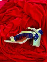 Sandalias de tacón cuadrado color azul eléctrico con acabado metalizado. Presentan una tira delantera y una pulsera al tobillo con hebilla ajustable. Decoradas con flecos metálicos plateados.