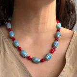 Collar corto con cuentas de cerámica ovaladas color celeste con líneas horizontales azules, alternadas con cuentas redondas rojas.