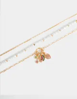 Collar corto dorado compuesto por tres cadenas de diferentes diseños: una de eslabones finos, una con perlas irregulares y otra de eslabones más grandes. Presenta dijes de frutas con strass de colores.