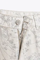 Pantalón de jean largo color crudo con estampado floral en gris, tiro medio, corte balloon y cinco bolsillos.