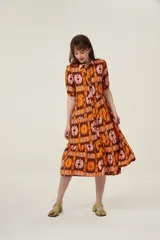 Vestido midi con estampado abstracto en tonos marrón, naranja y rosa. Tiene cuello camisero, mangas cortas abullonadas y falda escalonada con volantes.