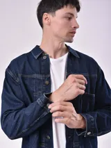 Campera de jean azul oscuro con cuello clásico, cierre frontal con botones metálicos y bolsillos en el pecho.