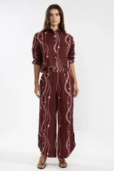 Camisa corta de lino color borgoña con estampado de cadenas y flores rosadas. Tiene cuello clásico, mangas largas y cierre frontal con botones.