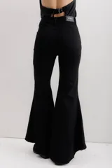 Pantalón de jean negro elastizado con corte ajustado y volados en la parte baja de la pierna. El ruedo es más largo en la parte trasera y tiene terminación descosida.