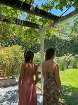 Vestido largo con escote en V, estampado en tonos rojizos y rosados, con un patrón ondulado. Presenta cut-outs laterales bajo el busto y breteles finos que se cruzan en la espalda.