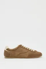 Zapatillas deportivas color marrón de piel con detalle de pespuntes, suela dentada, forro interior y parte trasera en contraste color crema. Cierre con cordones y acabado en punta redonda.