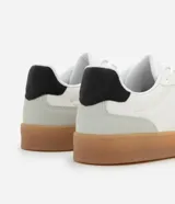 Championes urbanos de corte bajo, color blanco con detalles en gris y negro. Confeccionados en material sintético con recortes efecto gamuza y suela de látex color caramelo.