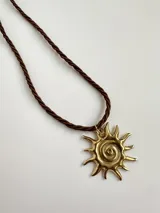 Collar con cordón trenzado marrón y dije dorado con forma de sol con espiral en el centro.