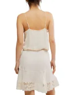 Top blanco con tirantes finos y escote en V, con detalle de bordado delicado en los bordes y abertura frontal con botones.