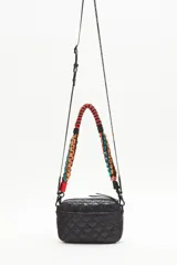 Bandolera negra de nylon matelassé con correa larga regulable y correa corta desmontable de cordones trenzados multicolores. Tiene cierre superior, bolsillo frontal con cierre, bolsillo trasero y dos bolsillos internos.