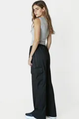 Pantalón negro de corte ancho con cintura elastizada y cordón ajustable. Presenta una franja vertical blanca a lo largo de la pierna y un bolsillo tipo cargo en el muslo.
