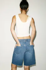 Bermuda de denim azul de tiro medio con cinco bolsillos, trabilla ajustable en la espalda, bajo sin costuras y cierre frontal con botones metálicos.