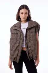 Chaleco puffer impermeable con estampado geométrico en tonos marrones y negros, forrado con tafeta negra. Tiene dos bolsillos frontales, bolsillos laterales ocultos, cierre desmontable, broches snap y elástico ajustable con tanca en ruedo.