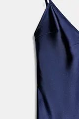 Vestido midi de satén color gris topo, con escote en V y tirantes finos regulables. El ruedo es asimétrico y está adornado con encaje. Cierre lateral con cremallera oculta.