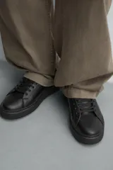 Zapatilla urbana de cuero sintético color negro, con cordones y suela de plataforma.