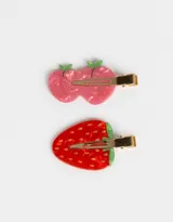 Set de dos hebillas para el pelo con forma de manzana rosa y frutilla roja, con detalles en verde y pinza dorada.
