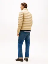 Campera acolchada de corte amplio, color beige, con cuello levantado y cierre de cremallera. Presenta dos bolsillos laterales ribeteados con cremallera y el logo de Tommy Hilfiger bordado en el pecho.