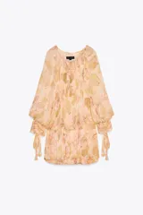Vestido corto con estampado floral en tonos pastel, cuello redondo con volantes y escote pico ajustable con lazadas. Manga larga acabada en puño con lazadas y bajo con pliegues.