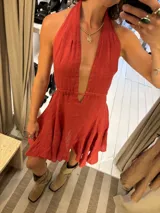 Vestido corto color marrón, con escote halter profundo en V y cintura marcada. La falda es acampanada y con vuelo.